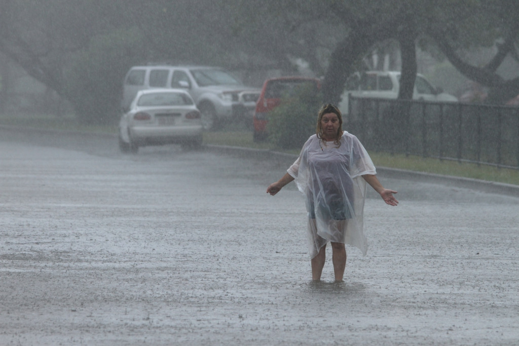 Photograph of a lady wearing a rain poncho and standing in the rain in the middle of a flooded road.